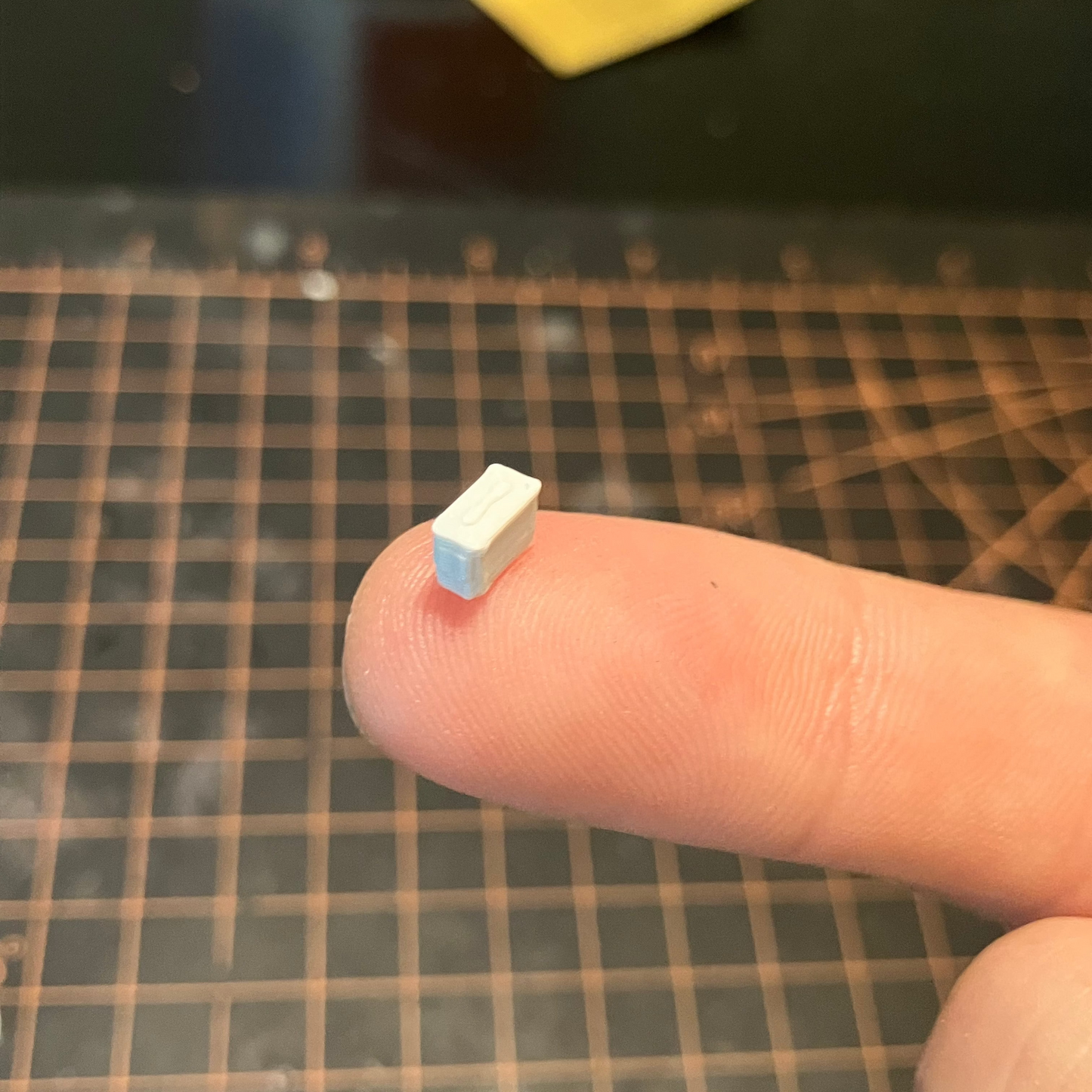 Small unpainted model of an ammo can on a finger over a grid surface with scattered pieces.