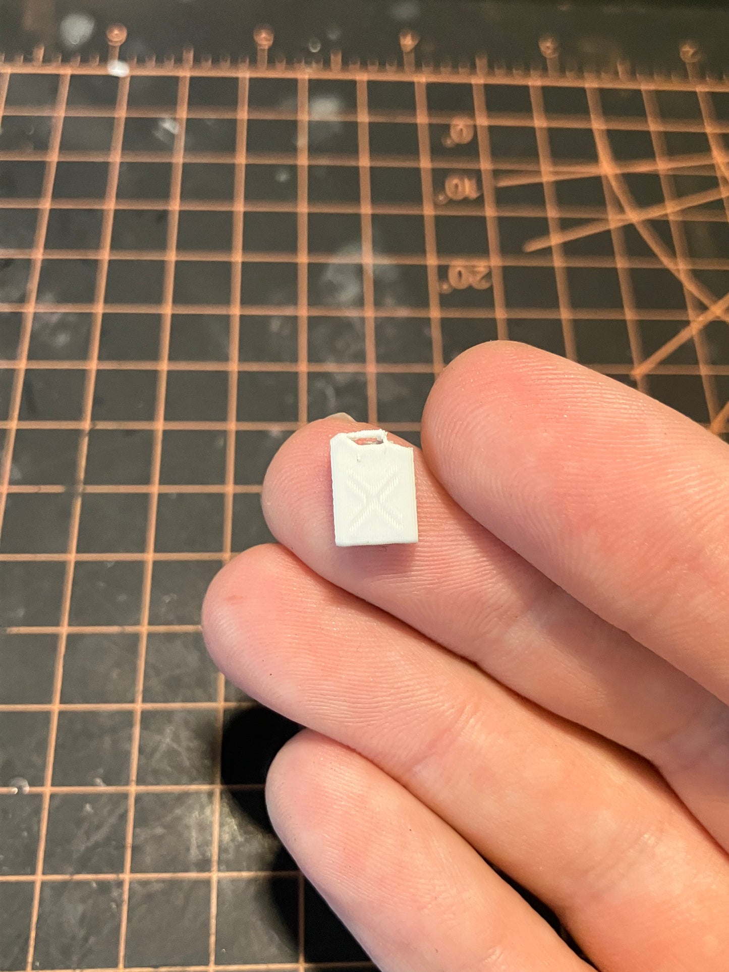 Small unpainted jerry can model held between fingers on a grid surface