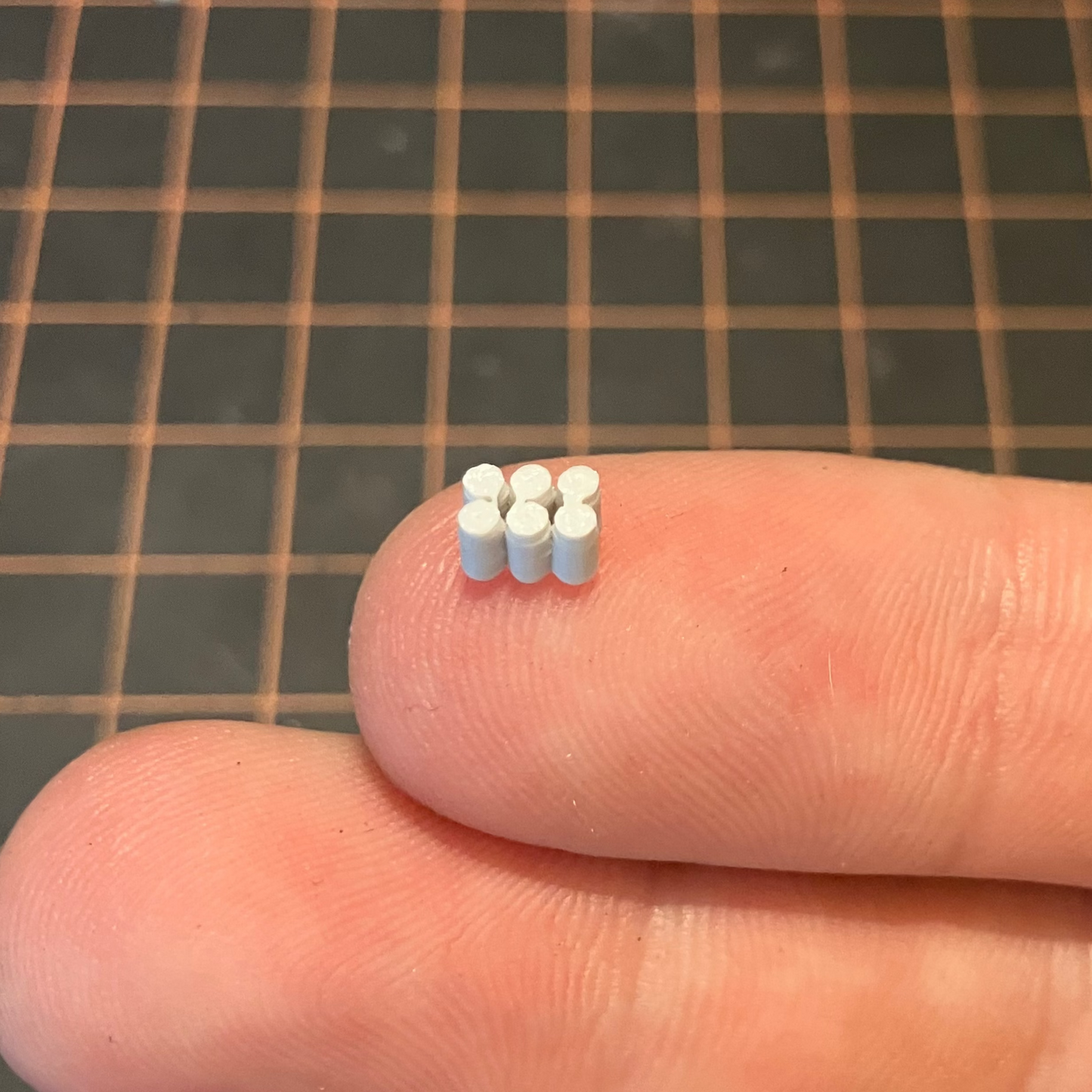 Small unpainted model beverage cans arranged on a person's finger with a grid-patterned surface in the background.